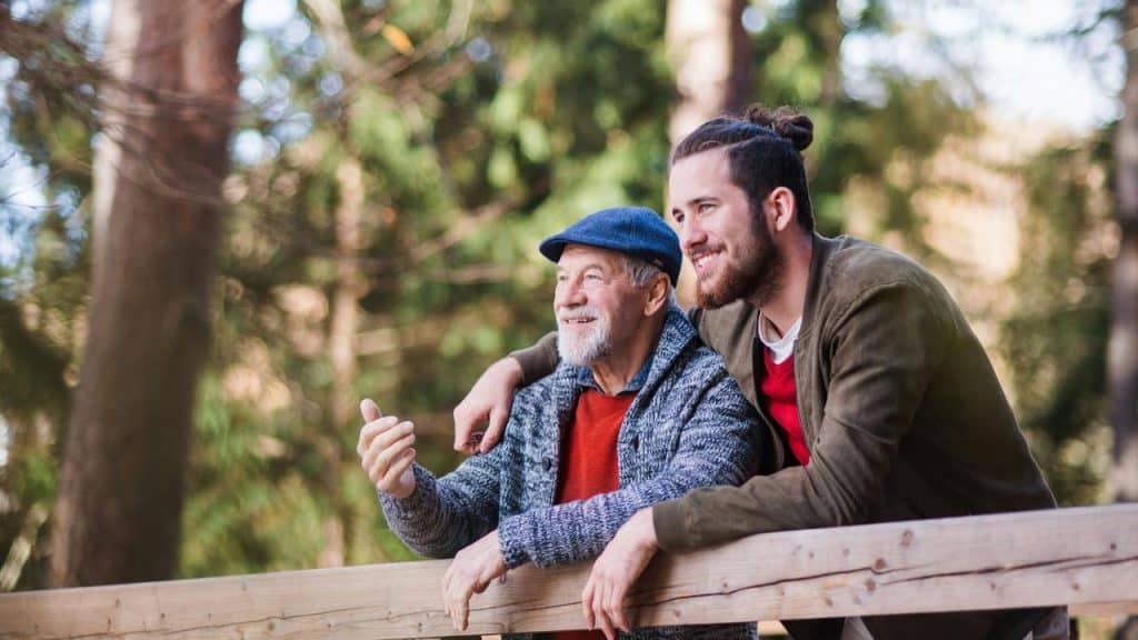 A young man and an older man leaning on a wooden railing outdoors.