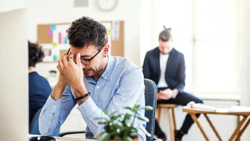 A tired man rubbing his eyebrows at his office desk.