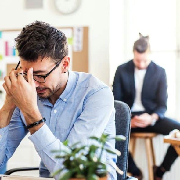 A tired man rubbing his eyebrows at his office desk.