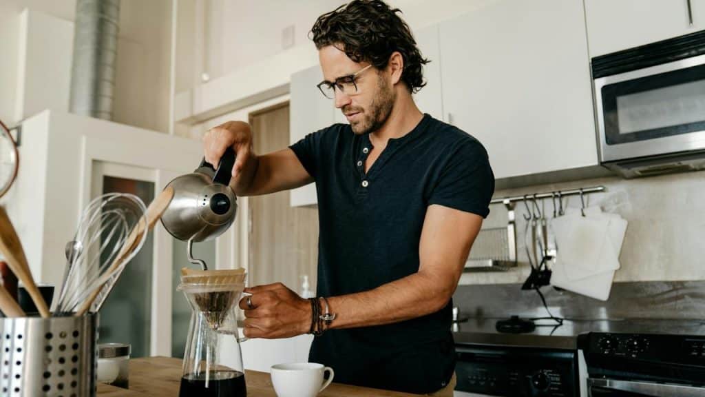 A man brewing pour‑over coffee in a kitchen.