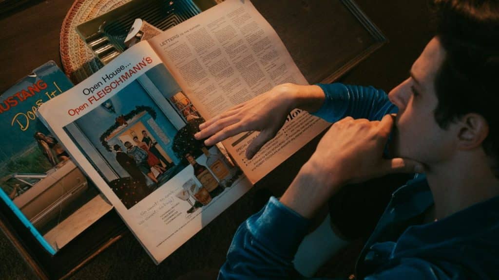 A person in a blue robe reads a vintage magazine with an advertisement for Fleischmann's on the left page.