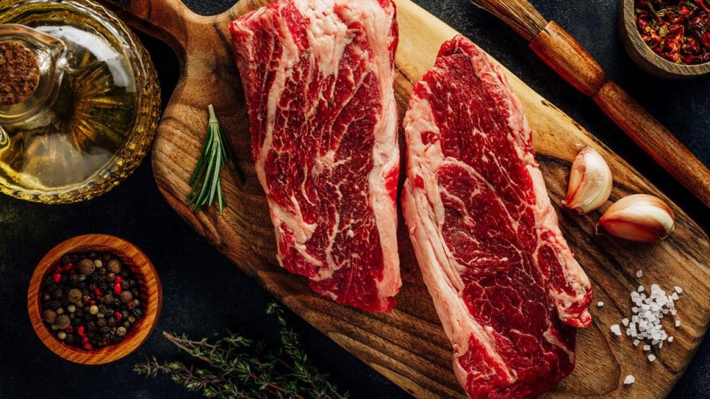 A top-down shot of two raw steaks on a wooden board with garlic and spices.