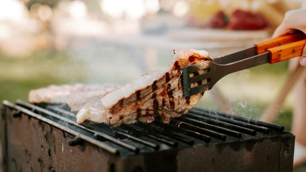 A pair of tongs flipping a piece of meat on a grill.