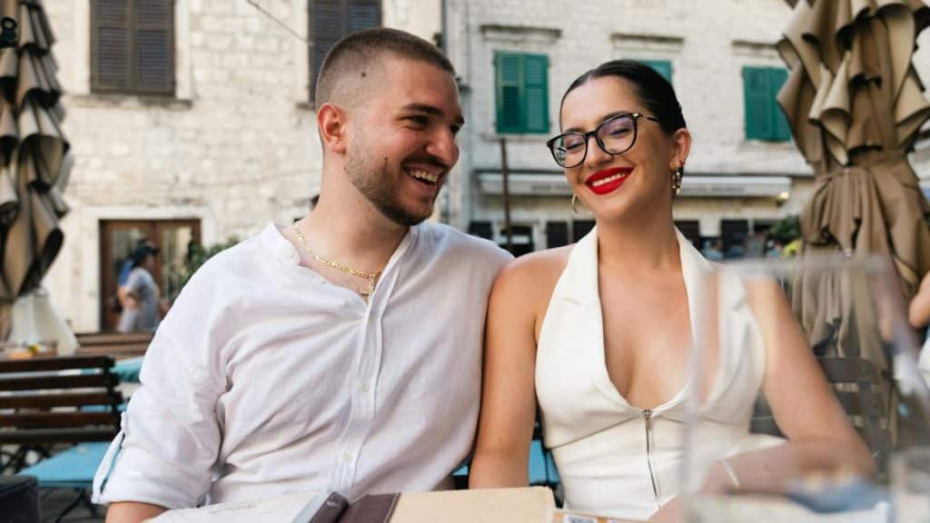A happy couple smiles at each other while seated at an outdoor cafe.