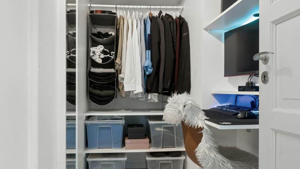 A neat closet with hanging clothes, storage bins, and a small desk with a computer.