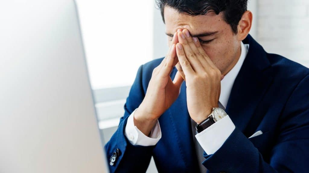 A man in a suit rubbing his eyes at his desk.