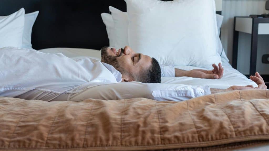 A man lying on his back in bed with arms stretched above his head.
