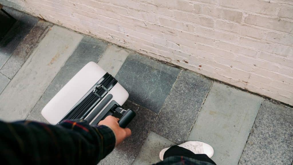 A person’s hand pulling a wheeled suitcase on a sidewalk.