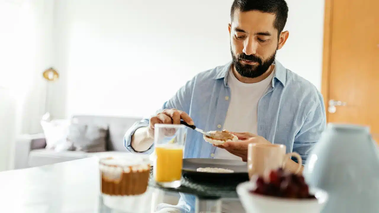 A man spreading nut butter on a bagel at a breakfast table.