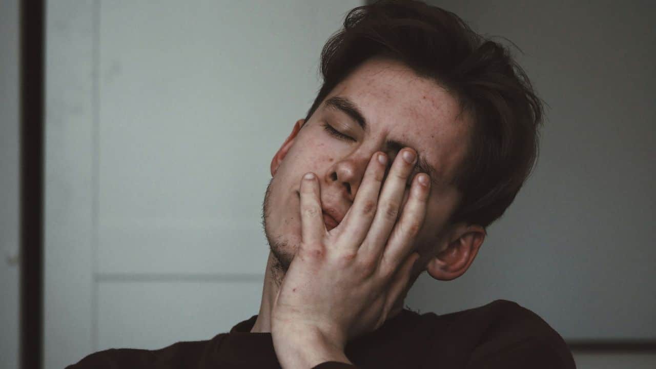 A young man covers his mouth with his hand, eyes closed, appearing stressed.