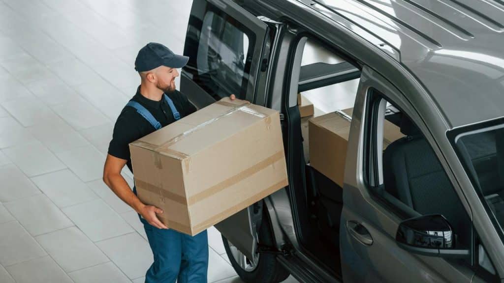 A delivery worker loading a cardboard box into a van.