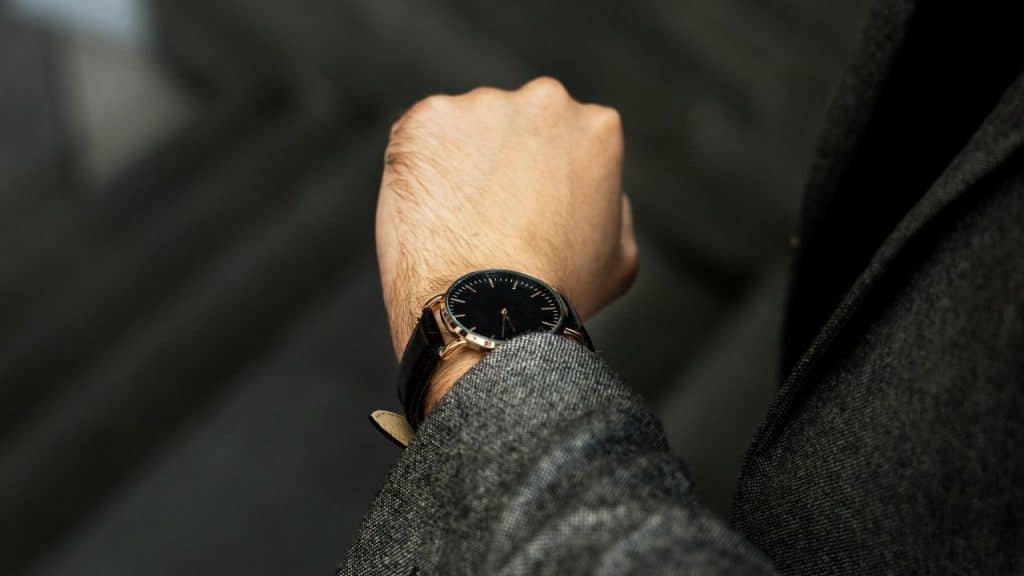 A man in a gray suit looks down at his wristwatch.