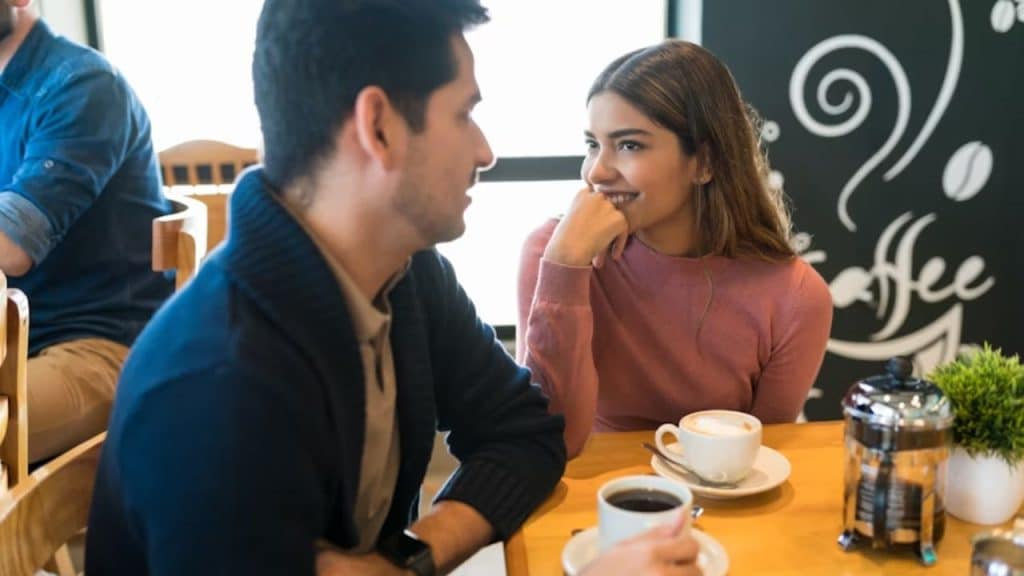 A woman smiling while making eye contact with a man at a coffee shop
