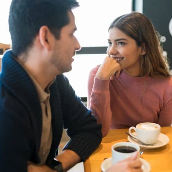 A woman smiling while making eye contact with a man at a coffee shop