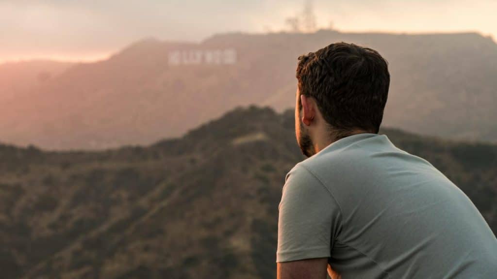 A man looking out over hills toward the Hollywood sign at sunset.