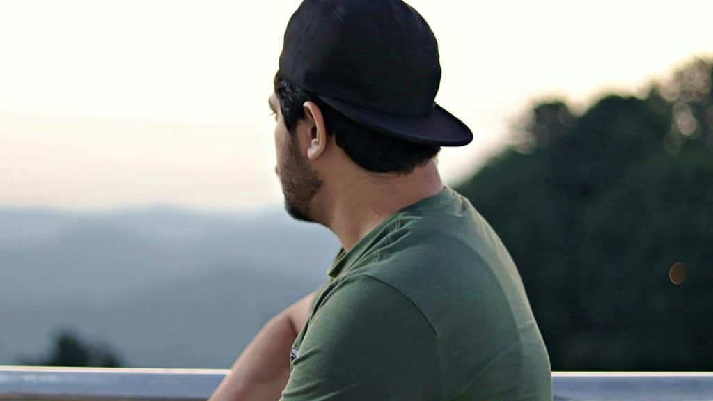 A man wearing a backwards cap looking out at misty mountains.