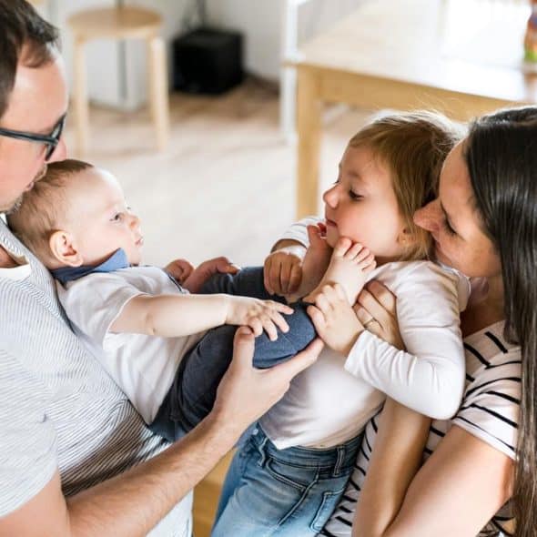 A mother and father holding a baby and a toddler at home.
