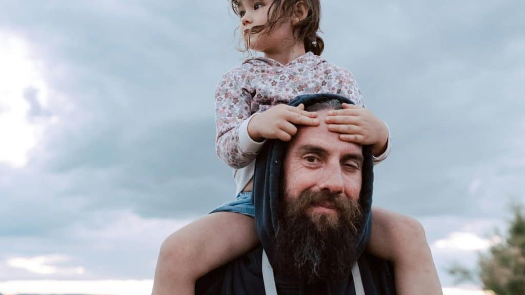 A bearded man carrying a child on his shoulders.