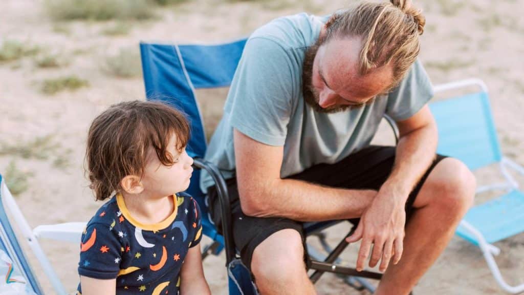 A man and a child sitting on outdoor chairs, the man leaning toward the child.