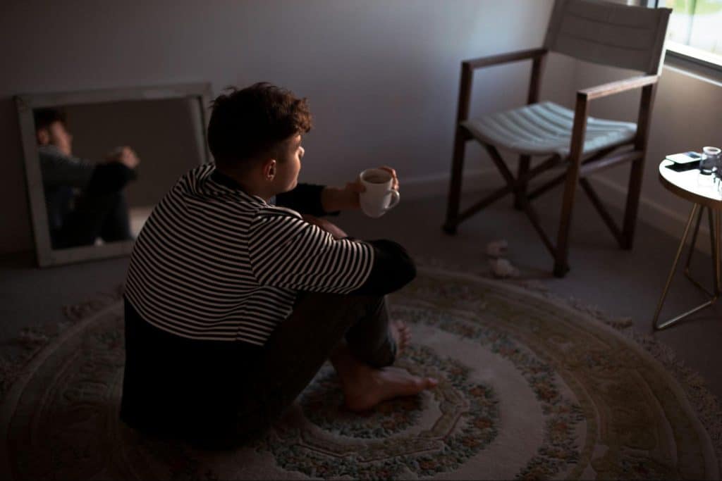 A man sitting alone at the rug while drinking coffee.