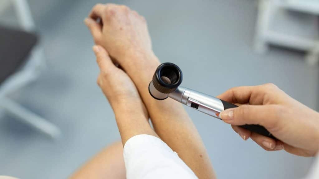 A hand holds a dermatoscopy tool over a person's forearm.