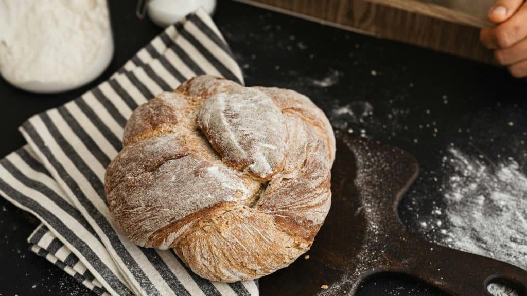 A round loaf of bread dusted with flour on a striped cloth and cutting board.