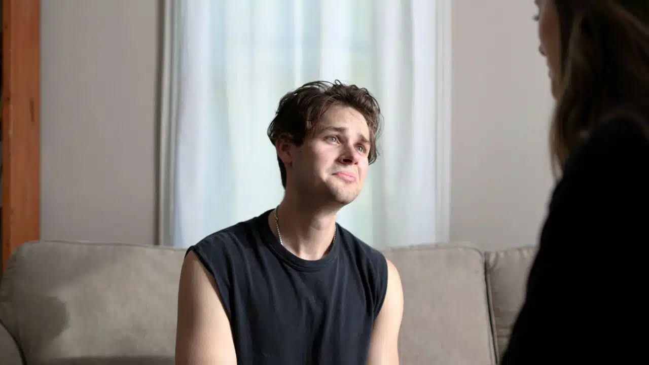 A crying man in a black tank top looks up at a woman.