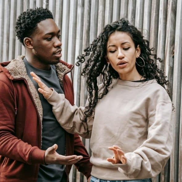 A man talks to a woman who is pushing him away with her hands.