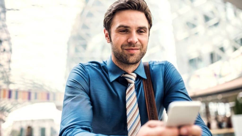 A man walking solo in a park while texting his partner with a smile