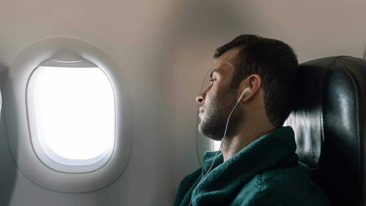 A man with earbuds looking out of an airplane window.