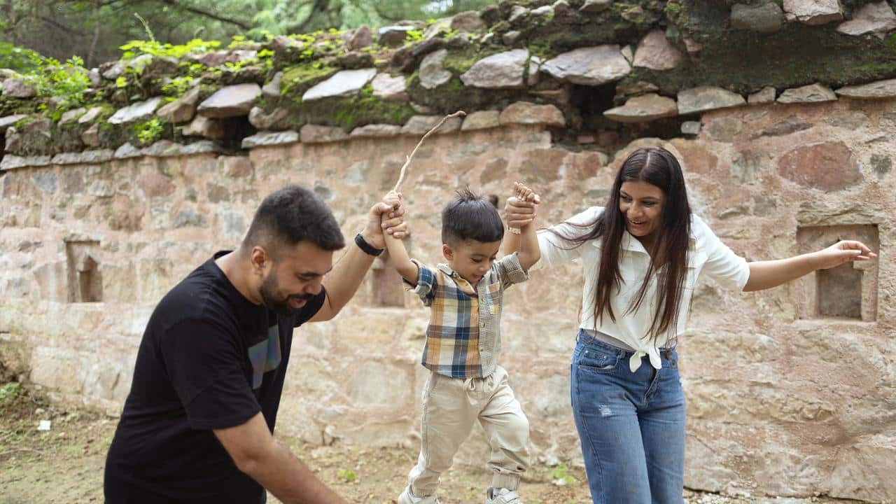 A child being swung between his parentsβ hands outdoors.