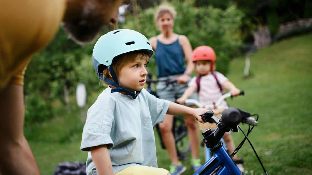 A boy wearing a helmet on a bicycle with family behind him.