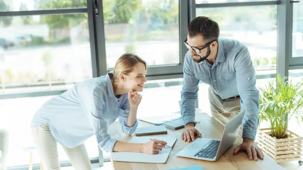 A man and woman collaborating over a laptop and notes.