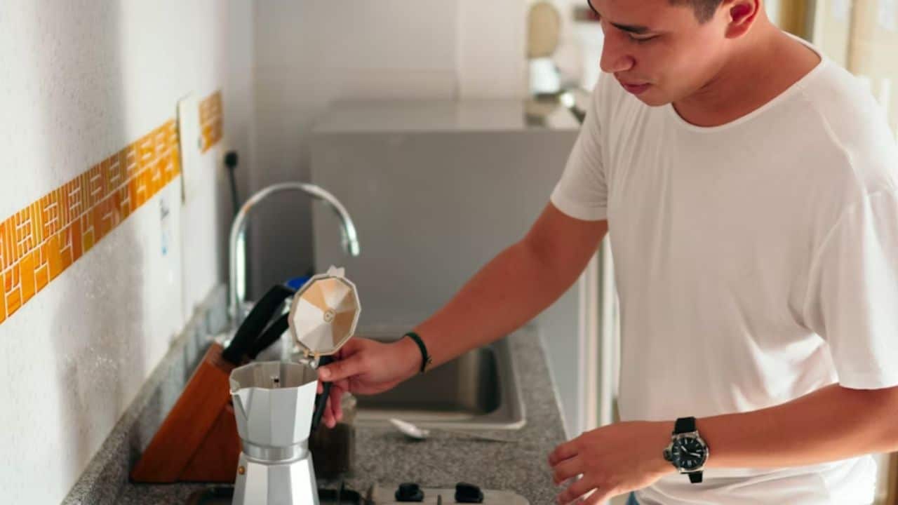 A man making coffee in a tidy kitchen as sunlight pours in.