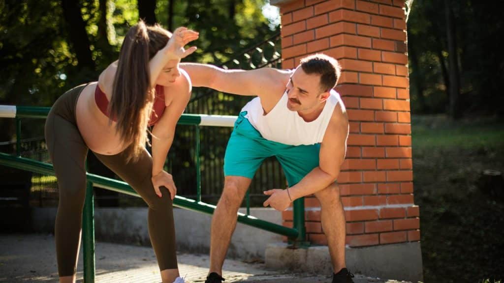 A man assisting his wife with a stretch outdoors.