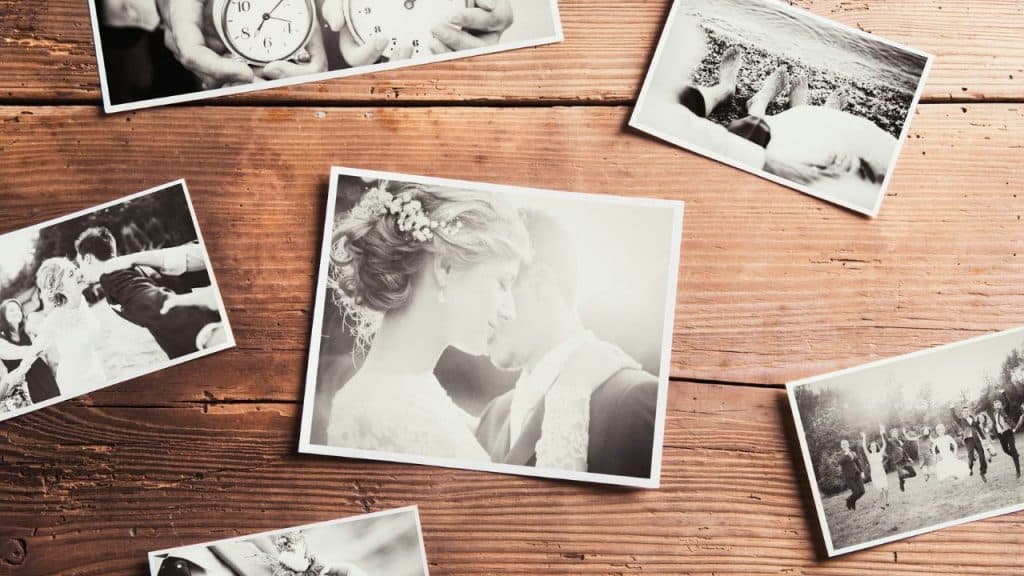 A top-down view of black and white wedding photos scattered on a wooden table.