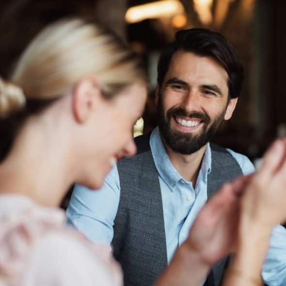 A bearded man smiling at a woman across a table.