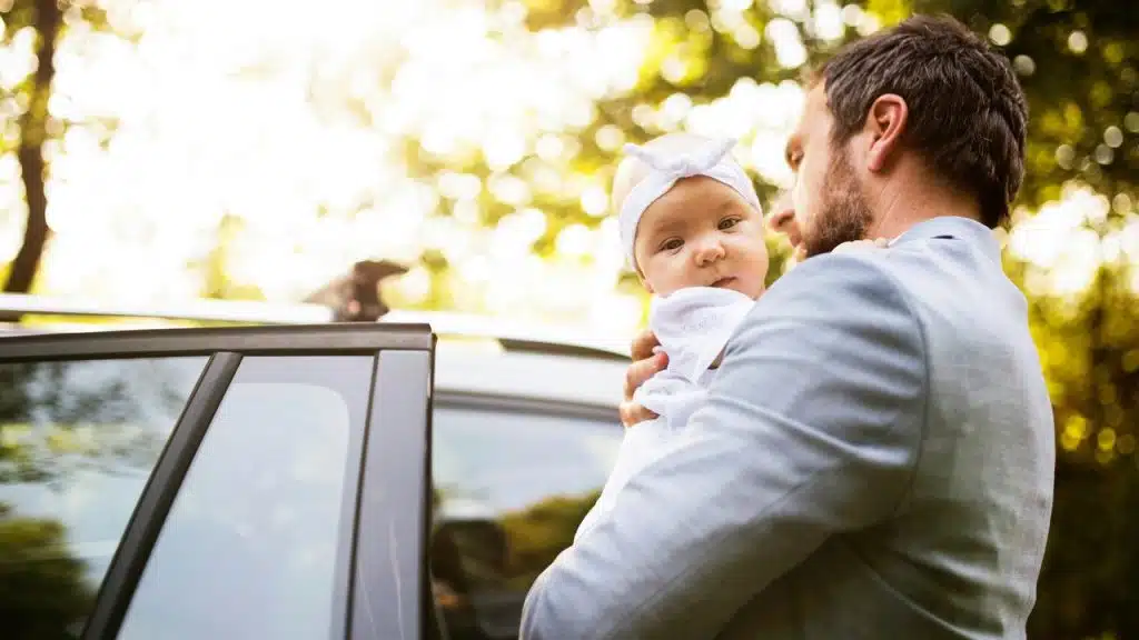 A man holding a baby beside a car door.