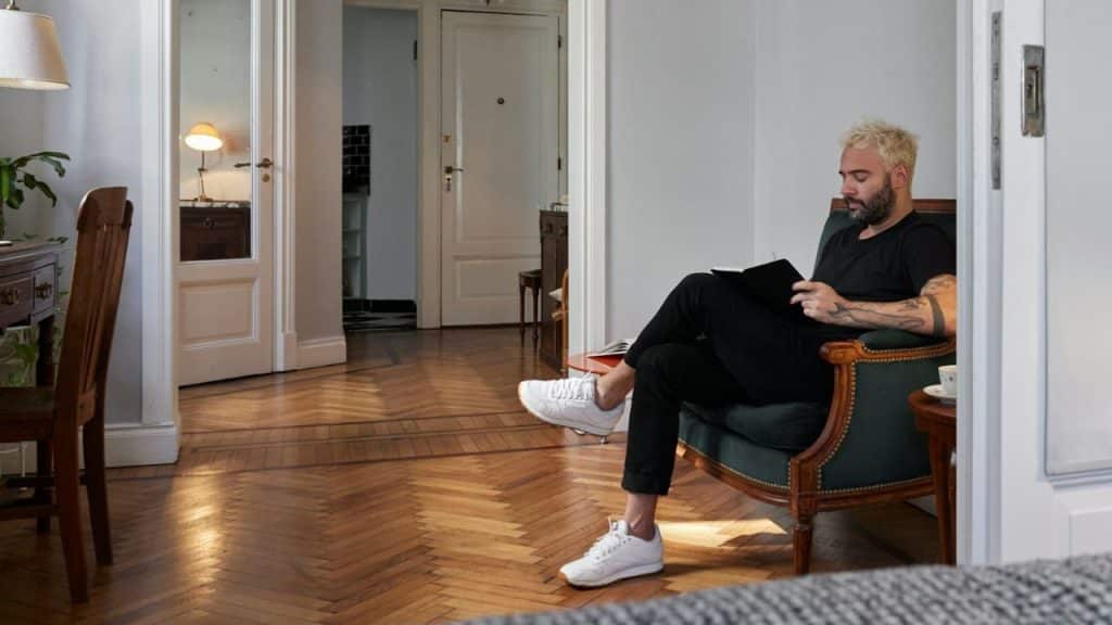 A man with blonde hair and a beard sits in an armchair, reading.