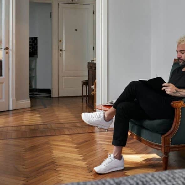 A man with blonde hair and a beard sits in an armchair, reading.