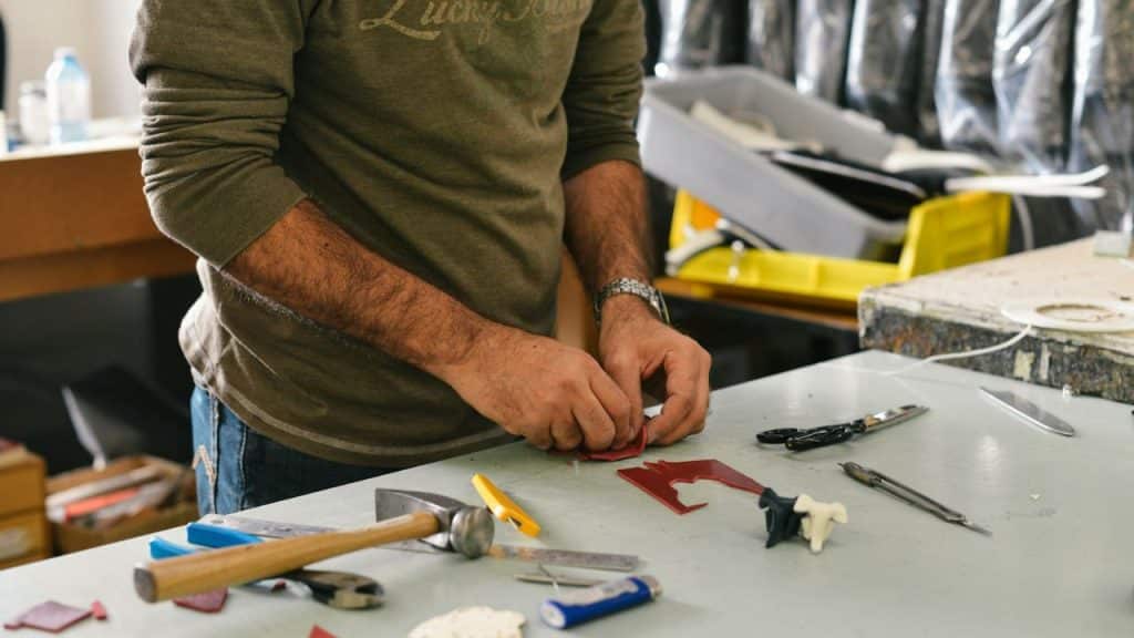 A man in a long-sleeved shirt is working on a craft project at a table with tools.