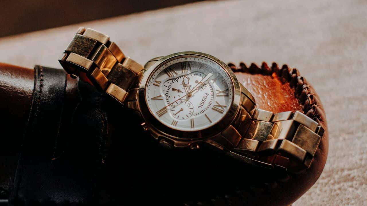 A gold Fossil watch with Roman numerals sits on a dark brown leather item.