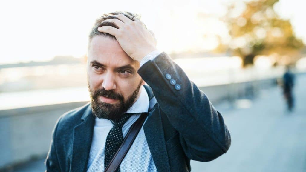 A man with a beard, wearing a suit jacket and tie, runs his hand through his hair.