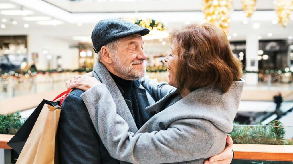 An older couple embracing in a mall with shopping bags.