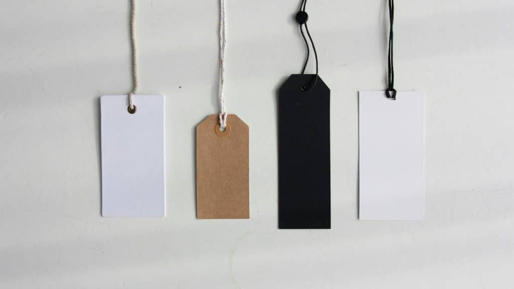 A row of four blank hanging tags in white, kraft brown, black, and white.