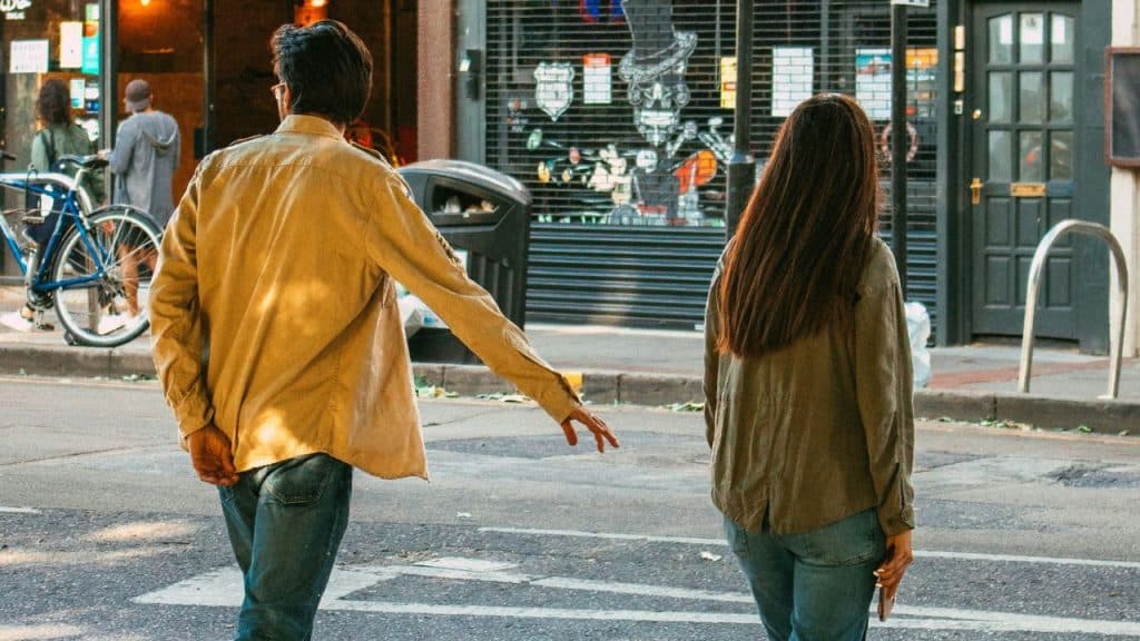 A man reaches out toward a woman walking away from him on a city street.