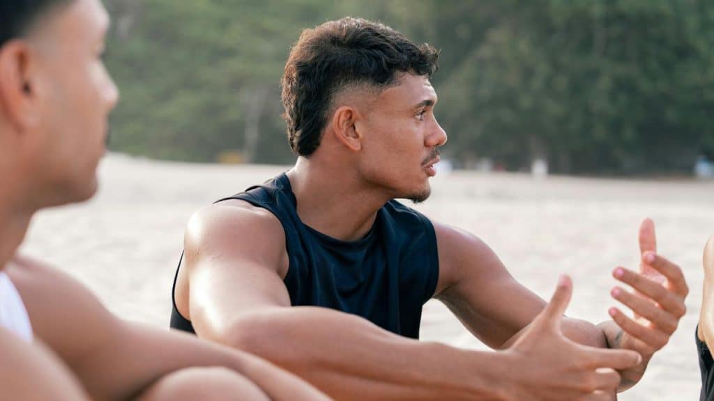 A man in a sleeveless shirt gesturing as he talks on a beach.