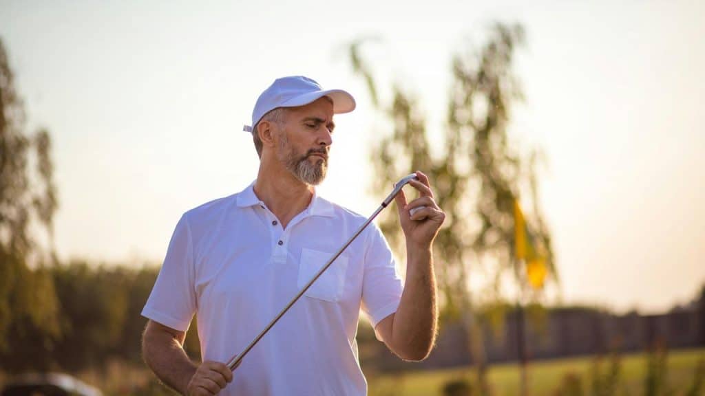 A man in white golf attire examining his club.