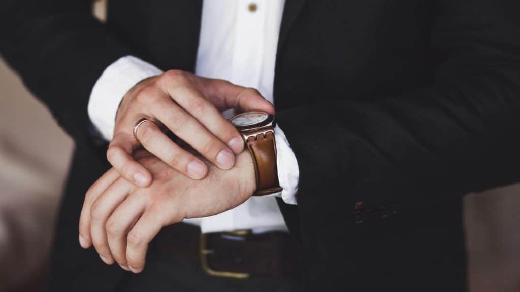 A man adjusting his wristwatch under a suit sleeve.