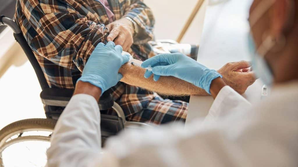 A gloved healthcare worker gives an injection to an elderly patient's arm.